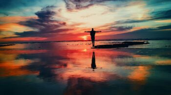 Image of a colorful sunset over water and a person standing with arms outstretched.