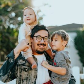 Image of man wearing glasses and holding two children in his arms.
