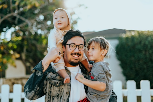 Image of man wearing glasses and holding two children in his arms.