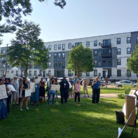 Group stands in park listening to a speaker.