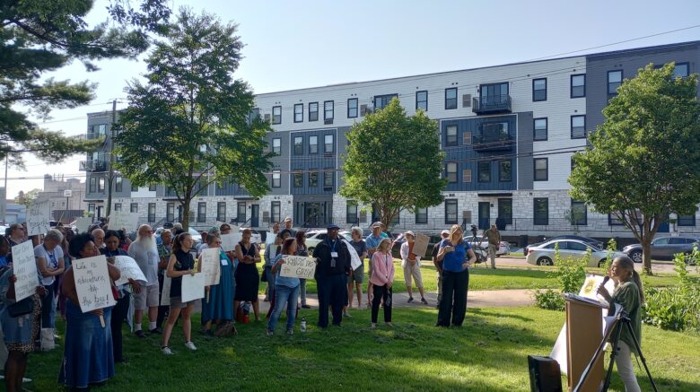 Group stands in park listening to a speaker.