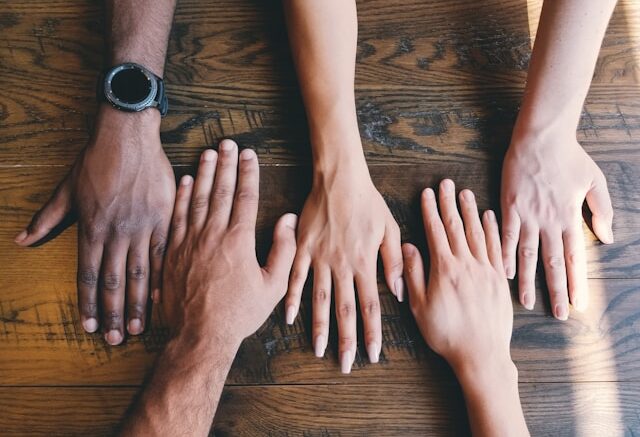 Image of five hands of different skin tones on a table side by side.