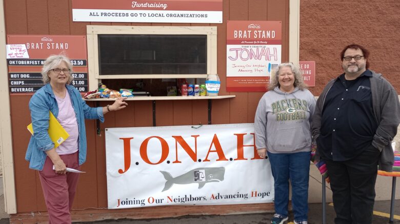 Image of three vollunteers in front of a brat stand. Sign says JONAH.