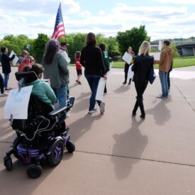Group of people march with signs and American flag.